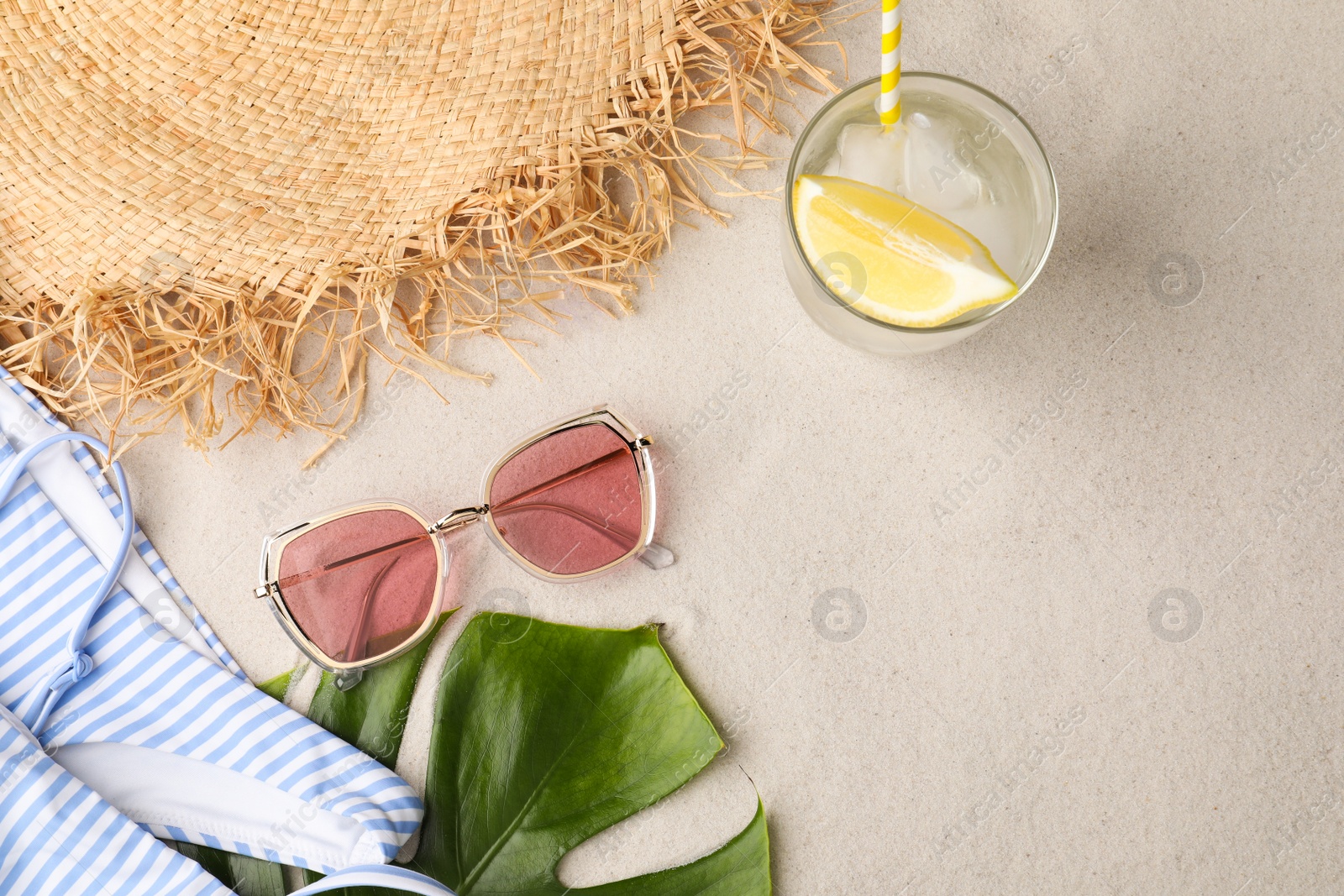 Photo of Stylish sunglasses, glass of refreshing drink and beach accessories on sand, flat lay