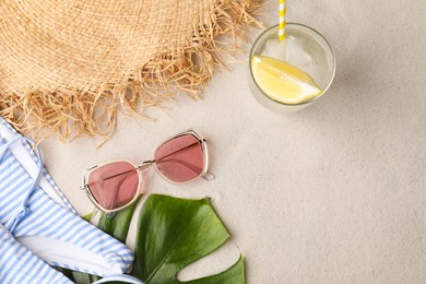 Photo of Stylish sunglasses, glass of refreshing drink and beach accessories on sand, flat lay