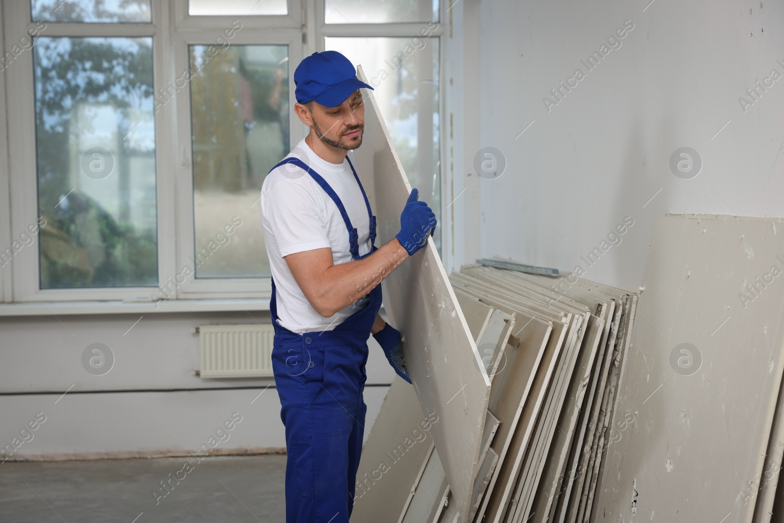 Photo of Construction worker carrying used drywall in room prepared for renovation