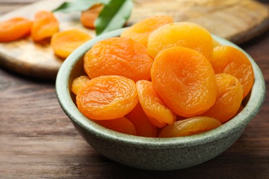 Photo of Bowl of tasty apricots on wooden table, closeup. Dried fruits