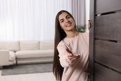 Photo of Happy woman welcoming near door, space for text. Invitation to come indoors
