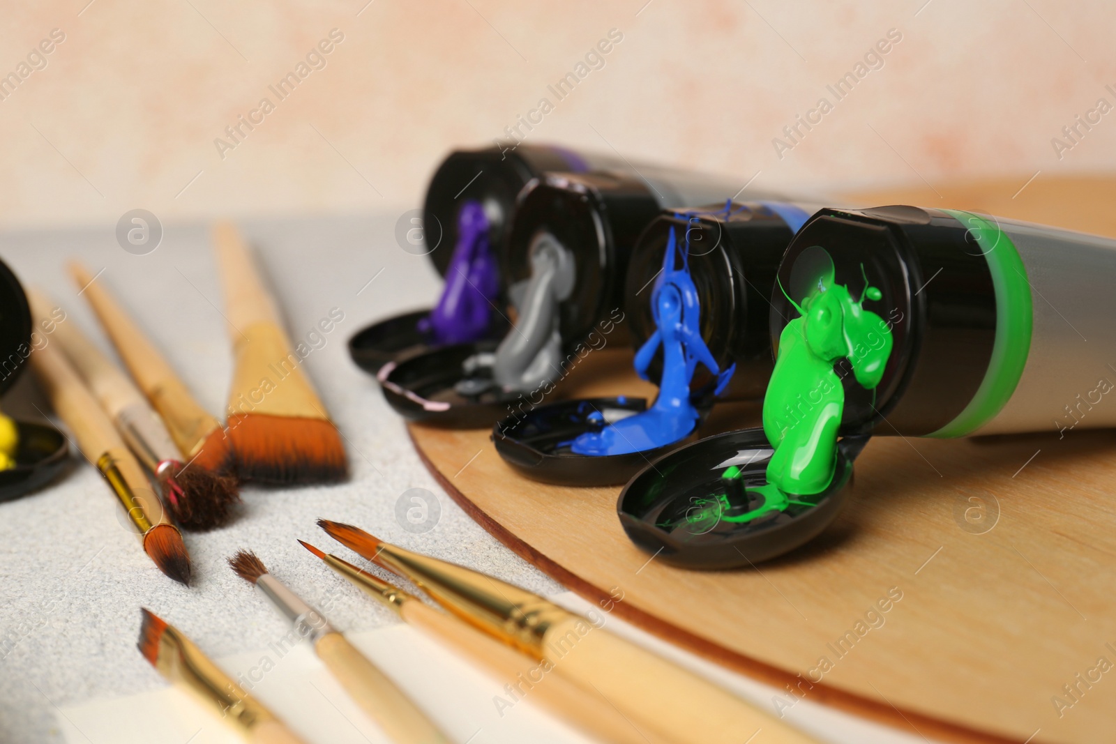 Photo of Tubes of colorful paints and brushes on textured table, closeup