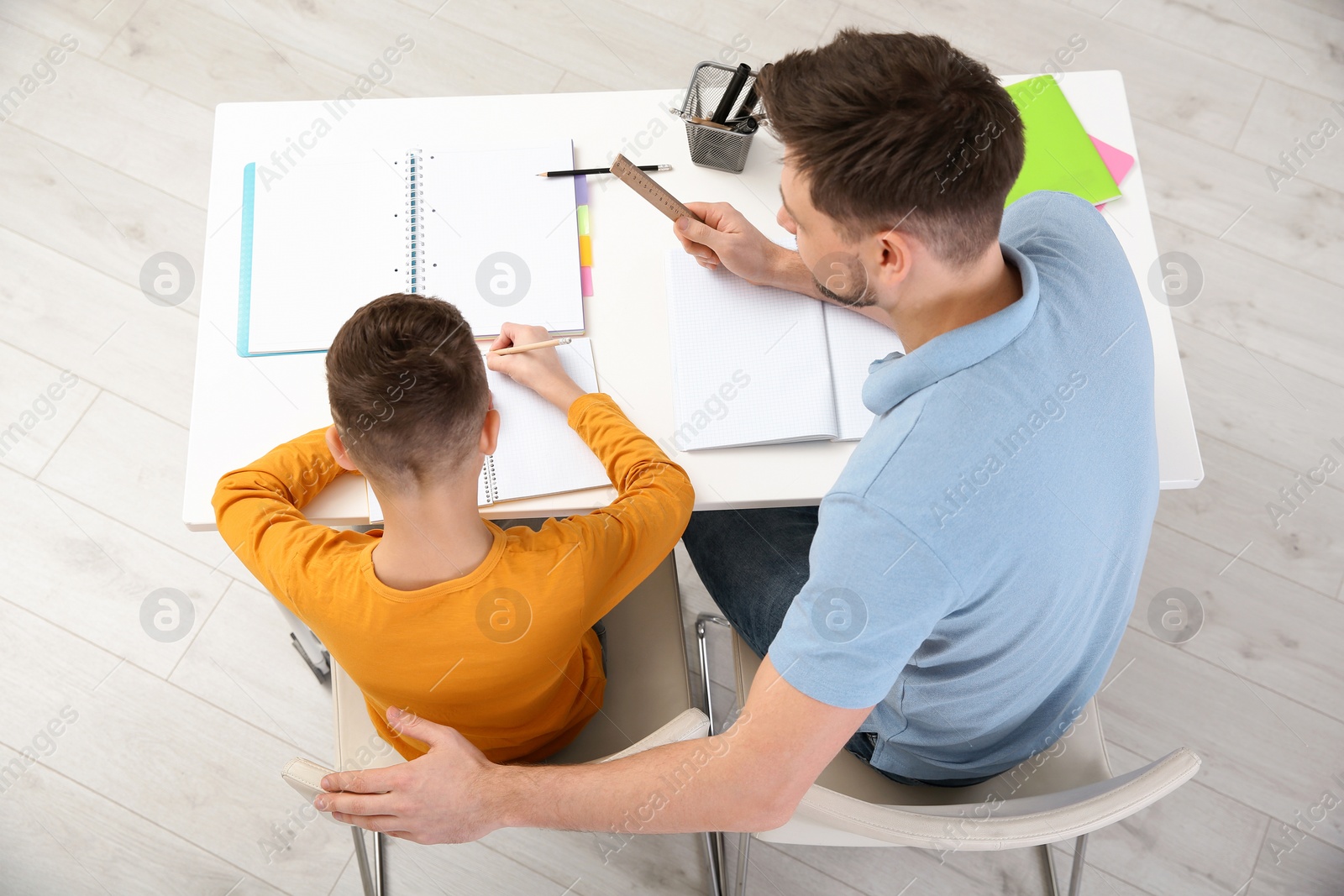 Photo of Dad helping his son with homework in room, above view