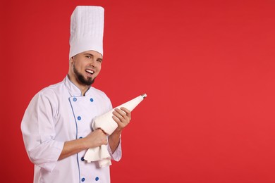 Photo of Happy professional confectioner in uniform holding piping bag on red background. Space for text