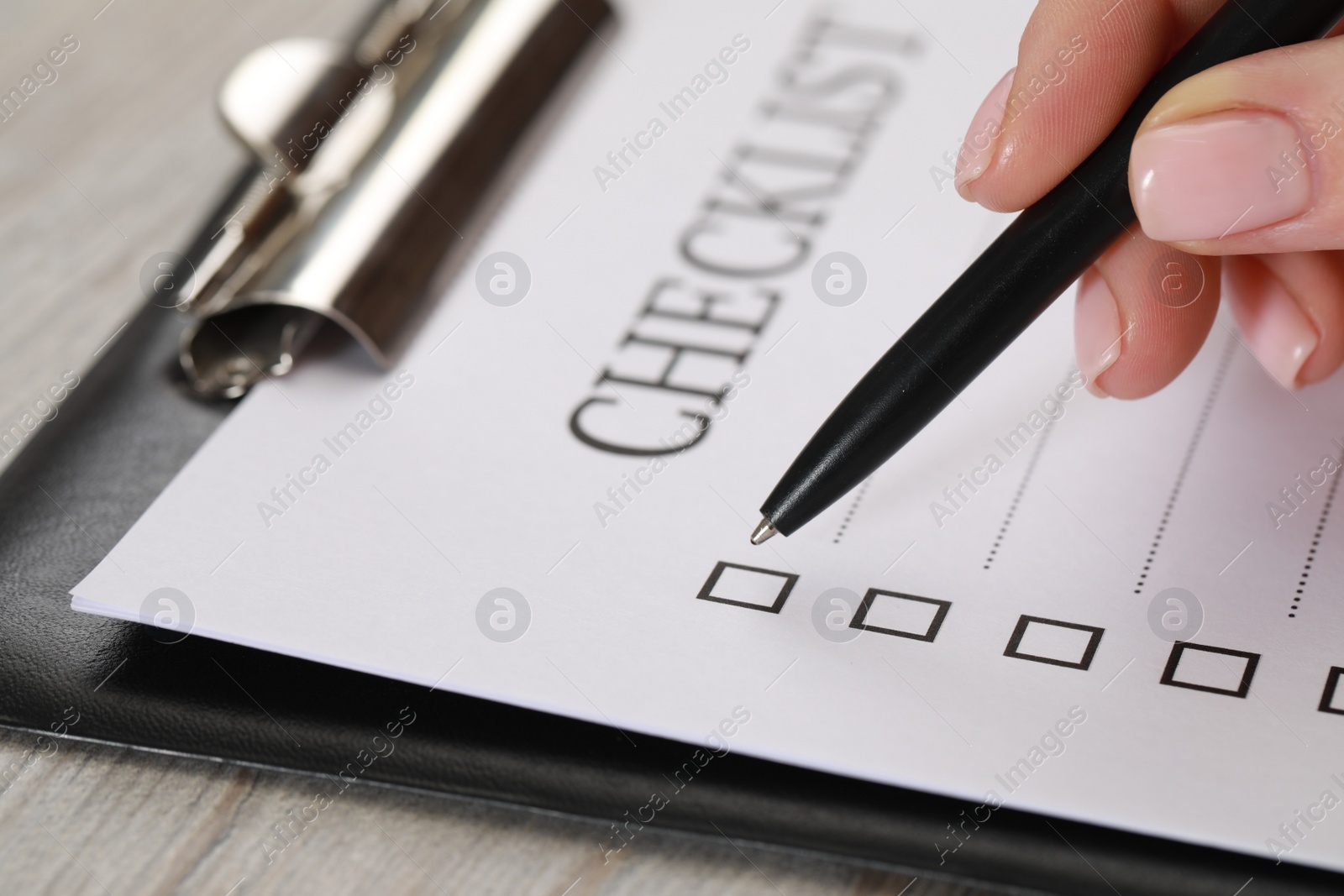 Photo of Woman filling Checklist at wooden table, closeup