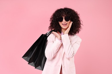 Photo of Happy young woman with shopping bags and stylish sunglasses on pink background