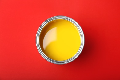 Photo of Can with yellow paint on red background, top view