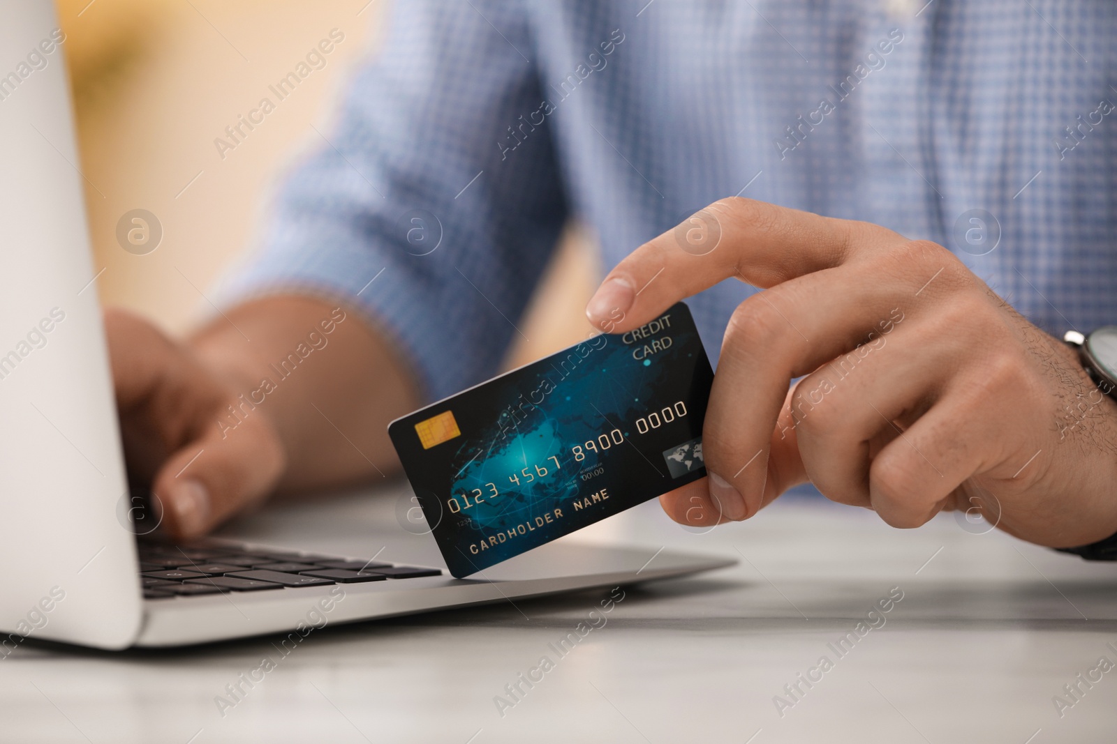 Photo of Man using laptop and credit card for online payment at table indoors, closeup