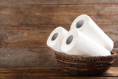 Photo of Rolls of paper towels in wicker basket on wooden table. Space for text