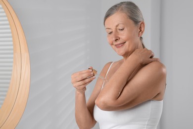 Photo of Happy woman applying body oil onto arm in bathroom. Space for text