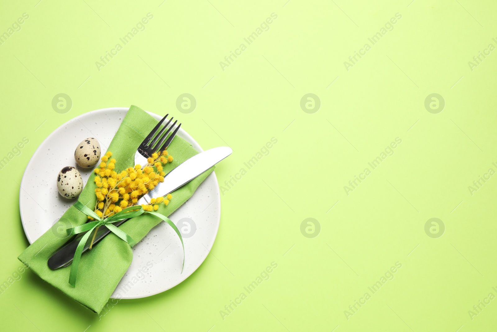 Photo of Festive Easter table setting with quail eggs and floral decor on green background, top view. Space for text