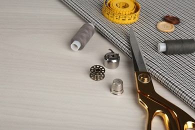 Photo of Composition with different sewing items and fabric on light beige wooden table