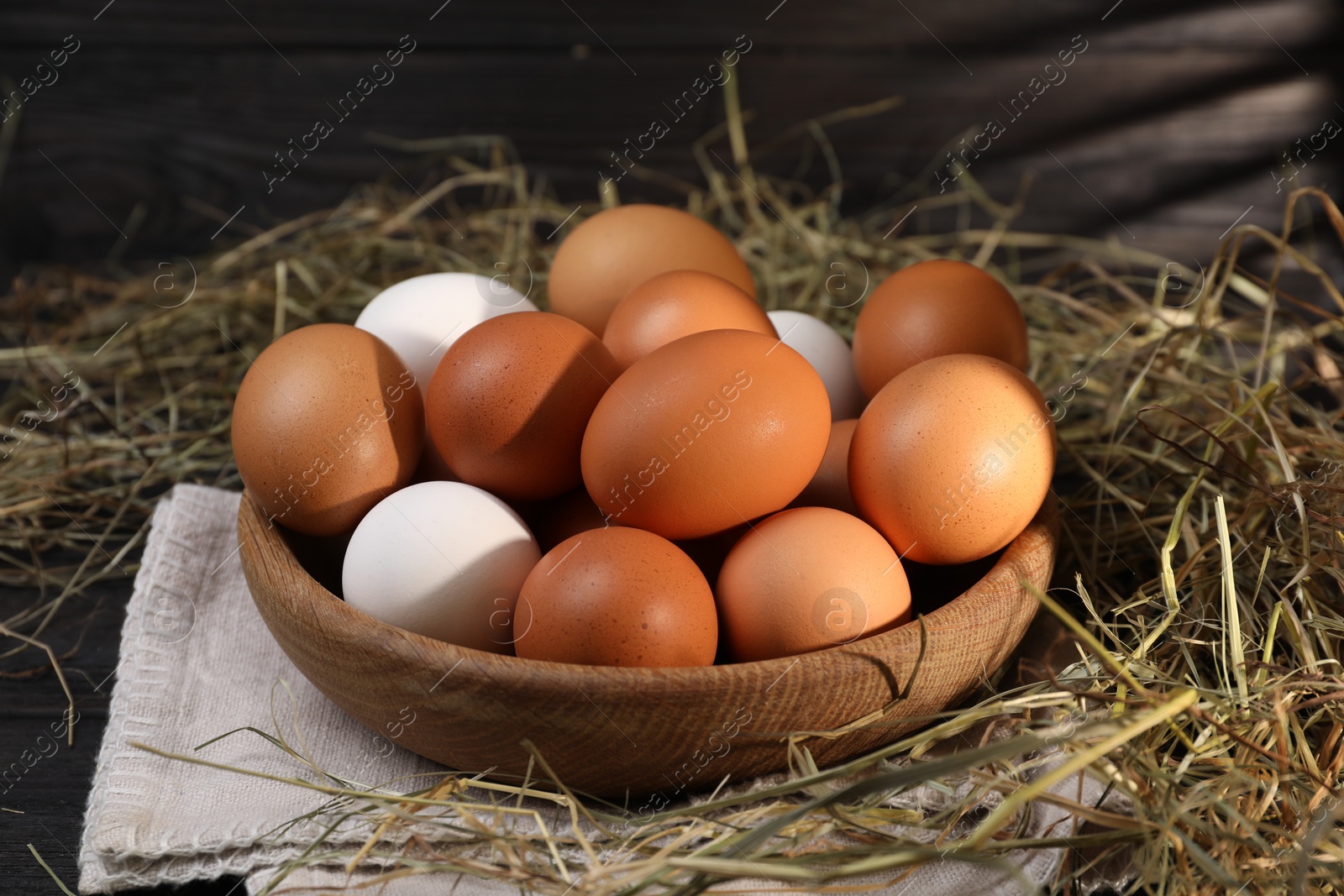 Photo of Fresh chicken eggs in bowl and dried hay on black wooden table