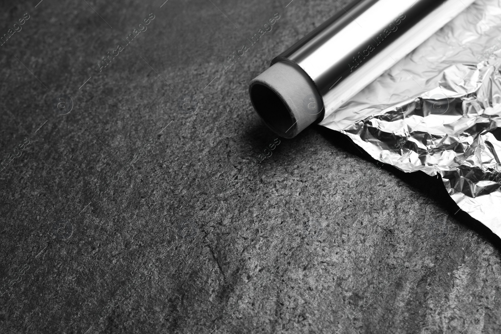 Photo of Roll of aluminum foil on grey table, closeup. Space for text