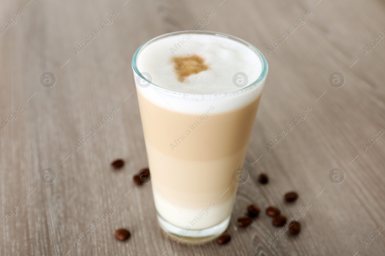 Photo of Delicious latte macchiato and coffee beans on wooden table