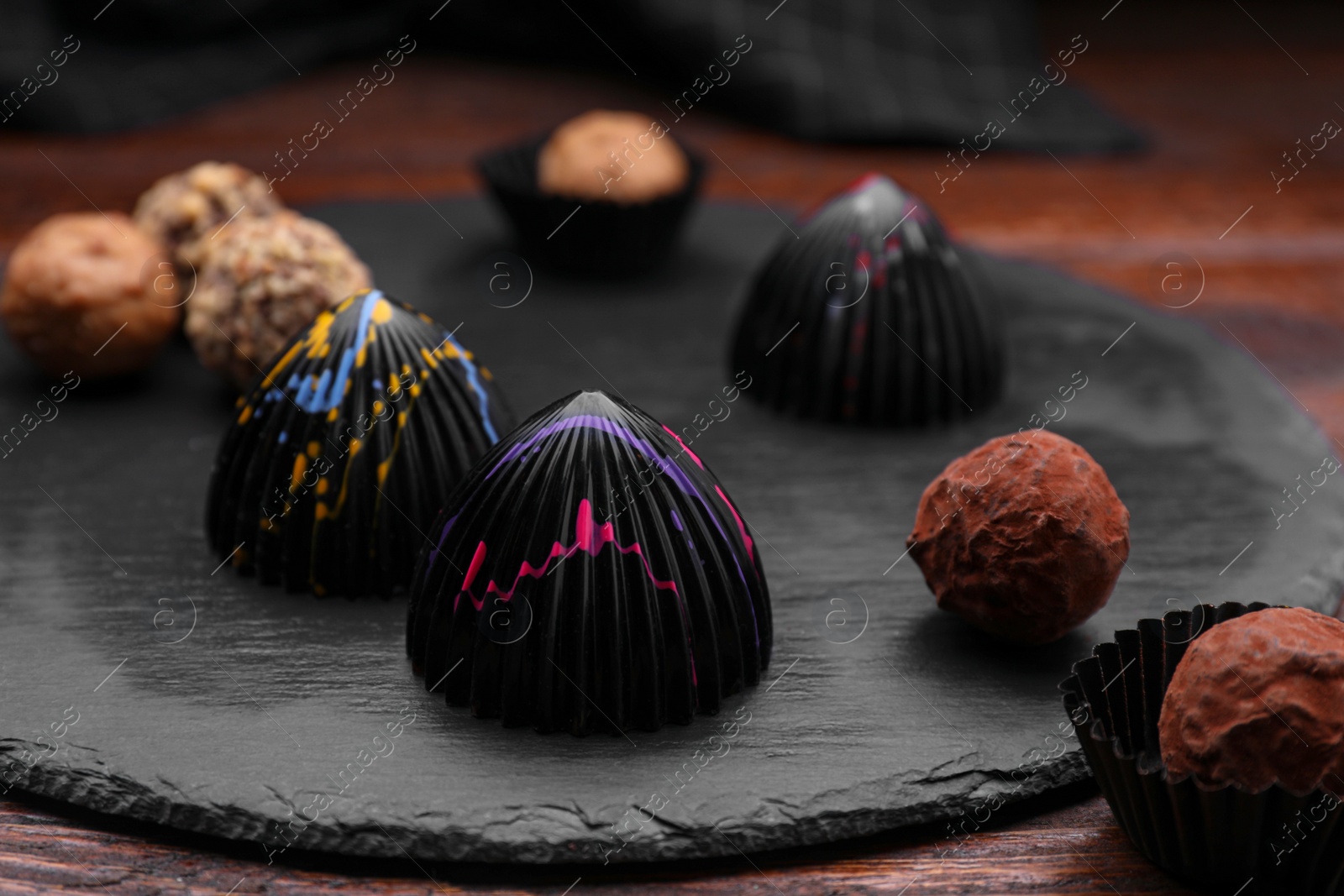 Photo of Different tasty chocolate candies on slate plate