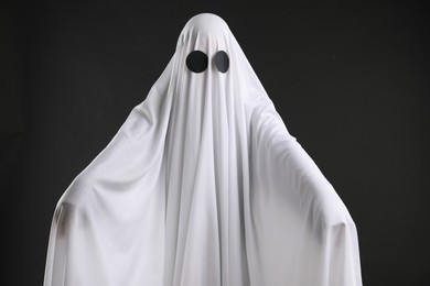 Photo of Creepy ghost. Person covered with white sheet on black background