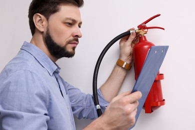 Man with clipboard checking fire extinguisher indoors