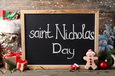 Blackboard with phrase Saint Nicholas Day, gift boxes and festive decor on wooden table