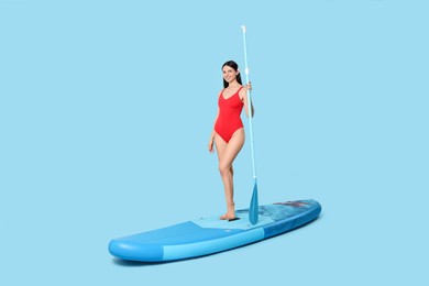Happy woman with paddle on SUP board against light blue background