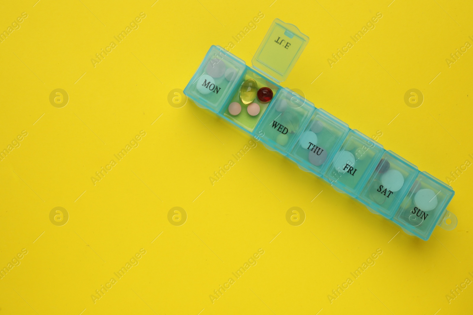 Photo of Plastic box with different pills on yellow background, top view. Space for text