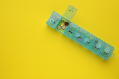 Plastic box with different pills on yellow background, top view. Space for text