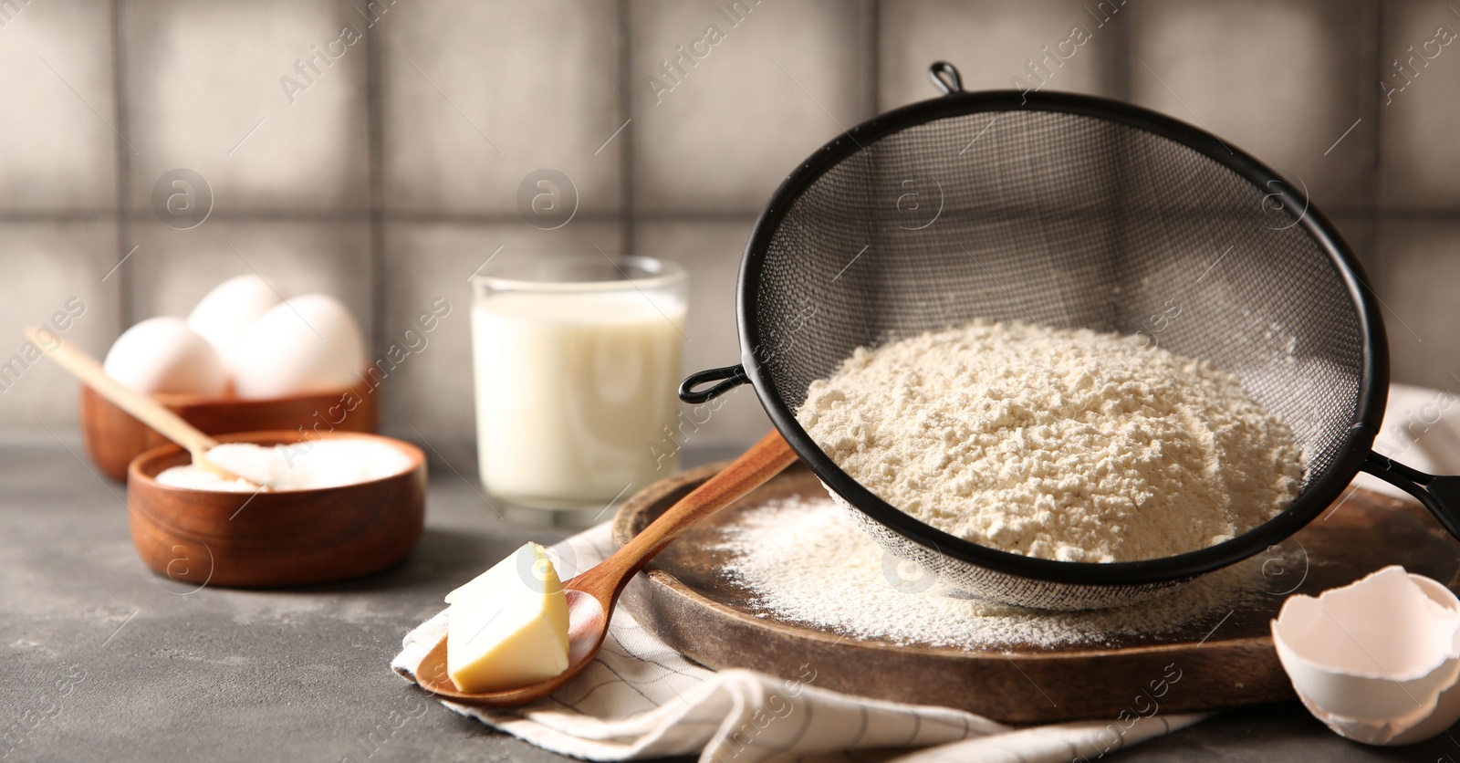 Photo of Making dough. Flour in sieve, spoon and butter on grey table, closeup