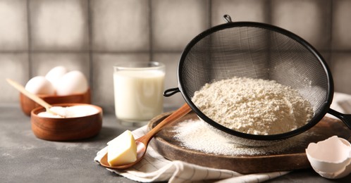 Photo of Making dough. Flour in sieve, spoon and butter on grey table, closeup
