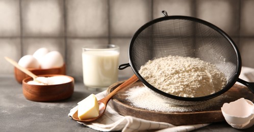 Making dough. Flour in sieve, spoon and butter on grey table, closeup