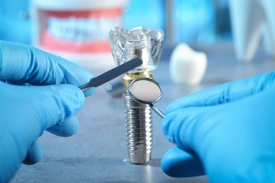 Dentist with tools pointing at educational model of dental implant indoors, closeup