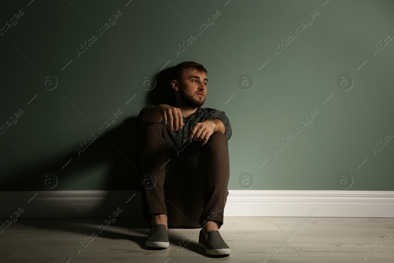 Photo of Depressed young man sitting on floor in darkness