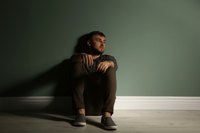 Depressed young man sitting on floor in darkness