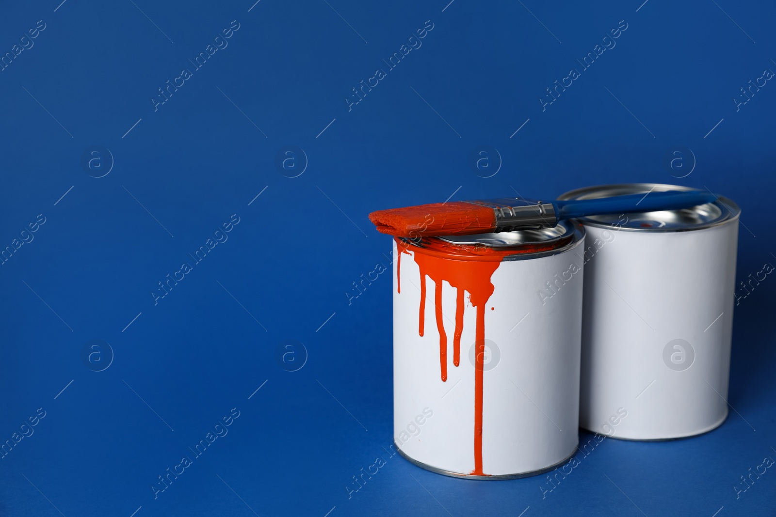 Photo of Cans of orange paint and brush on blue background. Space for text