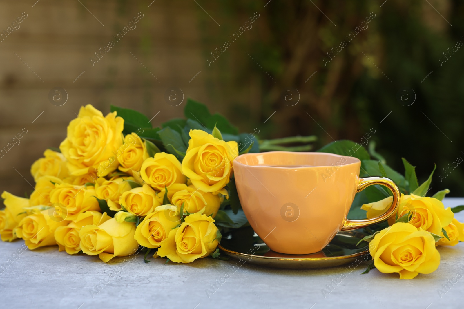 Photo of Cup of drink and beautiful yellow roses on light table outdoors, space for text