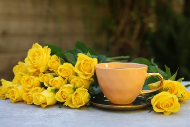 Cup of drink and beautiful yellow roses on light table outdoors, space for text