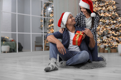 Photo of Happy young couple in Santa hats with Christmas gift at home
