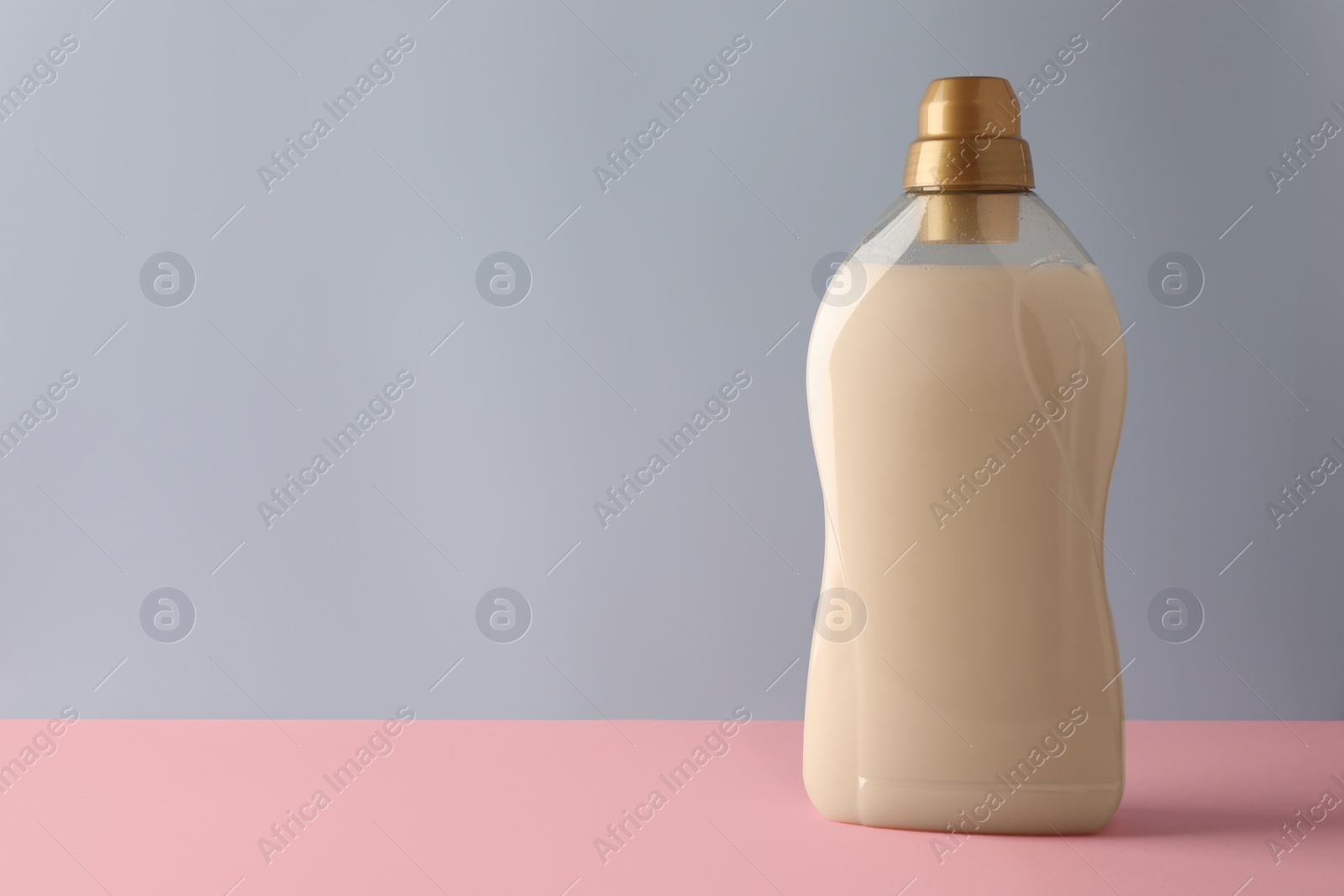 Photo of Bottle of fabric softener on pink table against light grey background, space for text