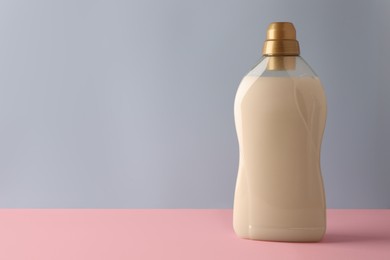 Photo of Bottle of fabric softener on pink table against light grey background, space for text