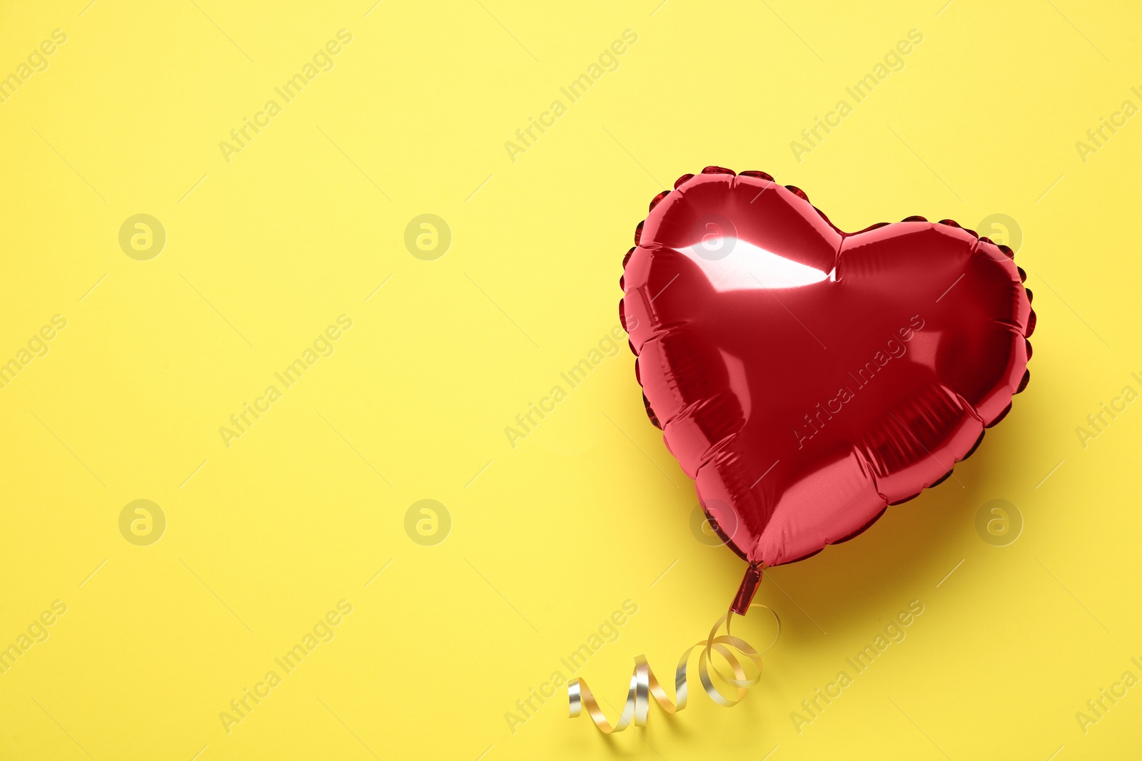 Photo of Red heart shaped balloon on yellow background, top view with space for text. Valentine's Day celebration