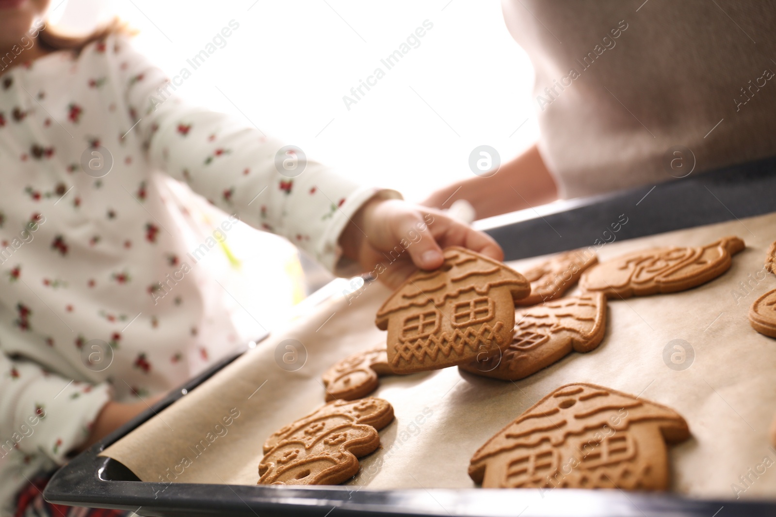 Photo of Little child taking tasty Christmas cookie from baking sheet at home, closeup