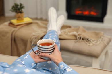 Photo of Woman with cup of tea resting near fireplace at home, closeup