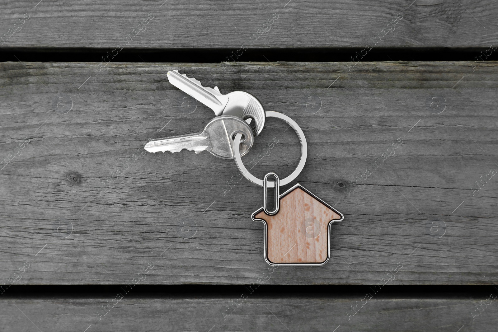 Photo of Keys with trinket in shape of house on wooden table, top view. Real estate agent services