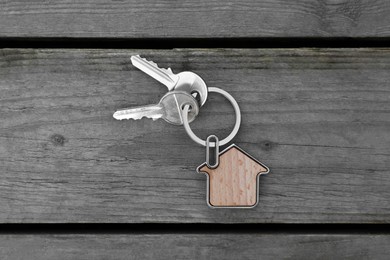 Keys with trinket in shape of house on wooden table, top view. Real estate agent services