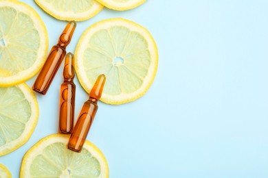 Skincare ampoules with vitamin C and slices of lemon on light blue background, flat lay. Space for text