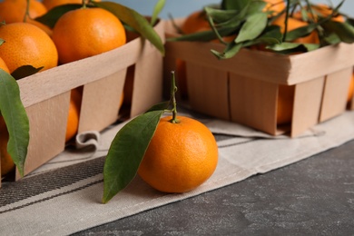 Photo of Fresh ripe tangerines with green leaves and crates on table