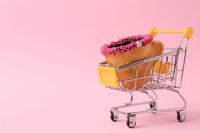 Photo of Delicious edible biscuit coffee cup decorated with sprinkles in shopping cart on pink background, space for text