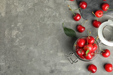 Glass jar with ripe sweet cherries on grey table, flat lay. Space for text