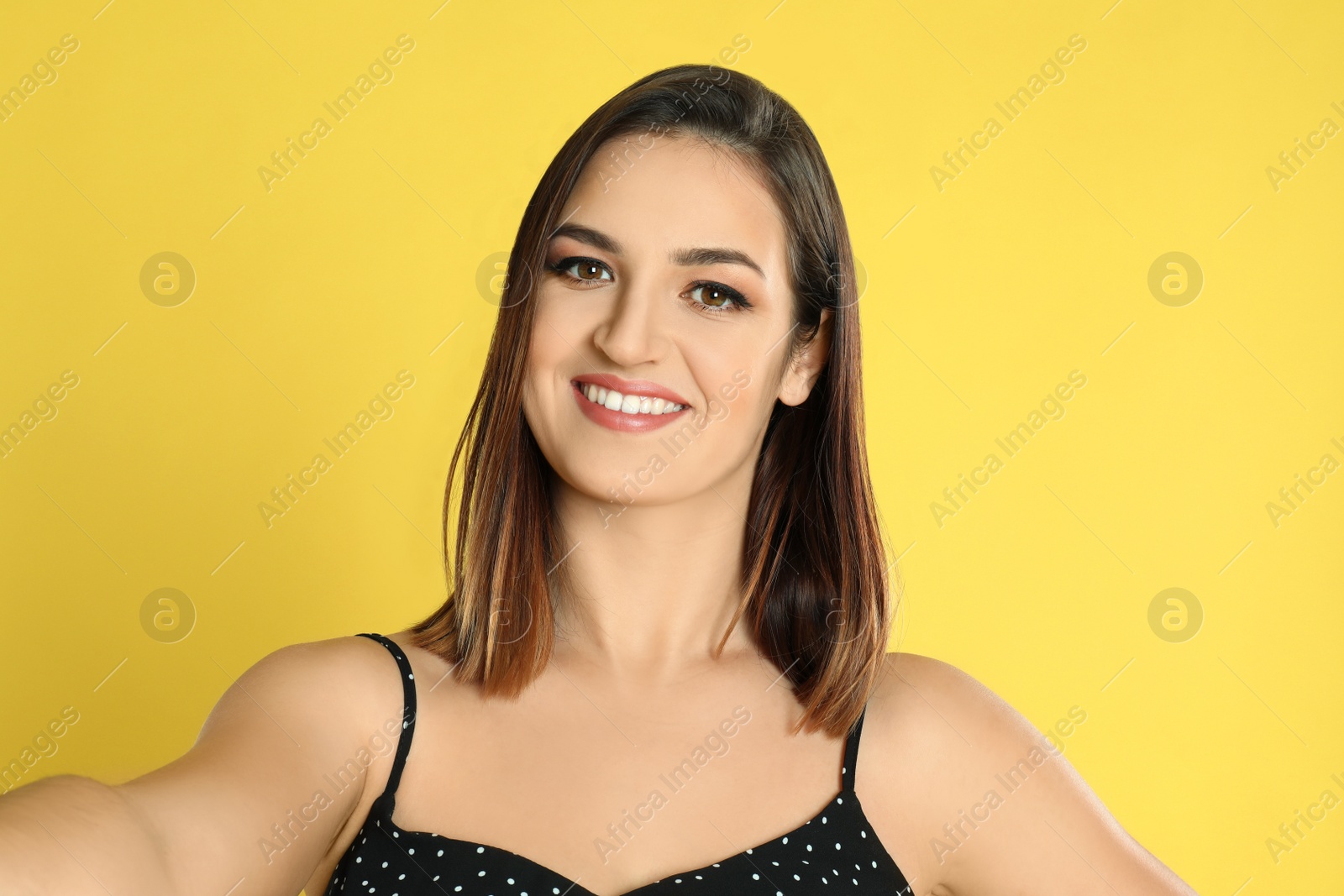 Photo of Beautiful young woman taking selfie on yellow background