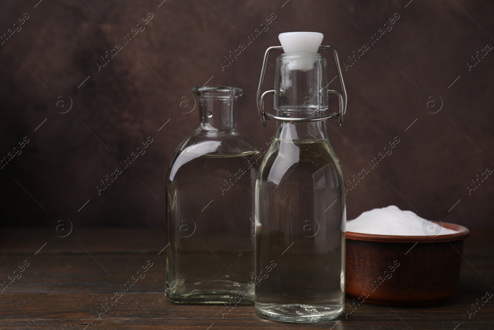 Photo of Vinegar in glass bottles and baking soda on wooden table, space for text