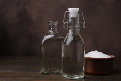 Photo of Vinegar in glass bottles and baking soda on wooden table, space for text